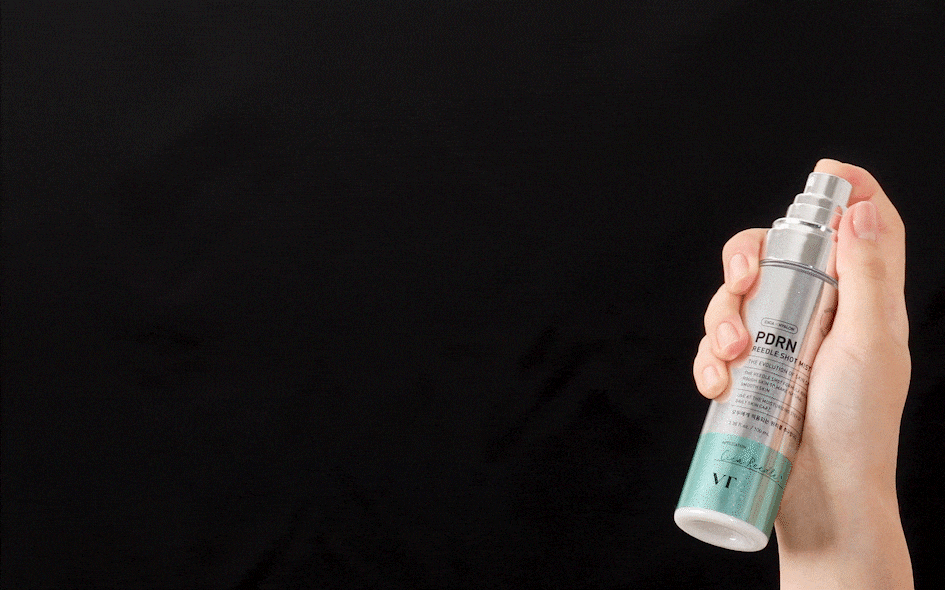 Hand holding VT PDRN Reedle Shot Mist 100ml and pressing the spray nozzle, showing the mist against a dark background.