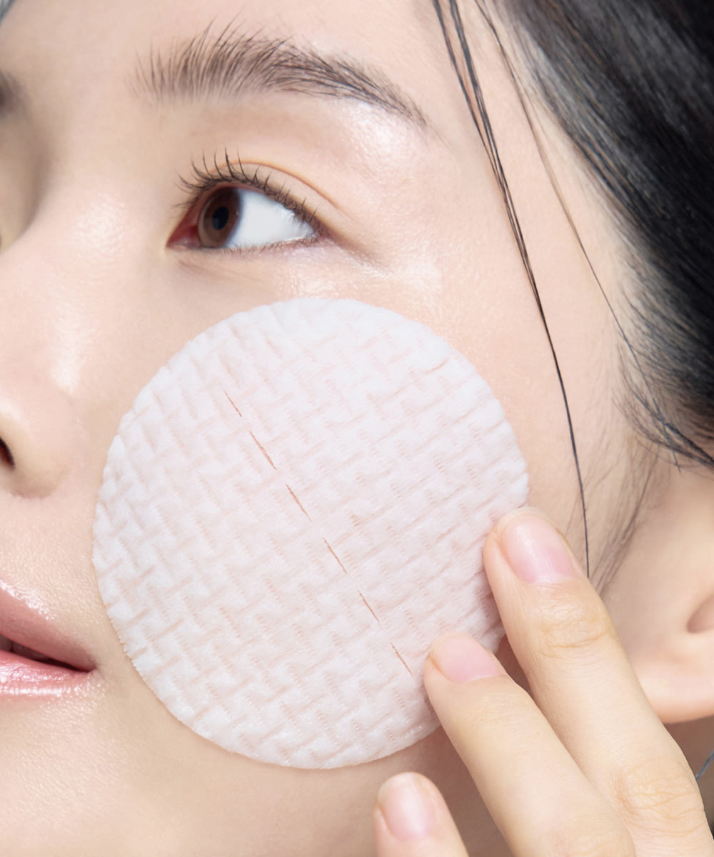 Disco CELIMAX Ji Woo Gae Cica BHA Blemish Toner Pad sobre una mejilla, con su forma redonda y superficie texturizada visibles