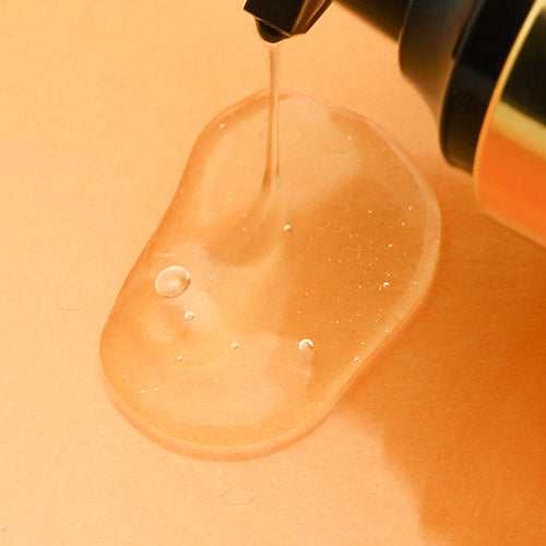 Elizavecca CER-100 Hair Muscle Essence Oil dispensing from a black pump onto an orange surface