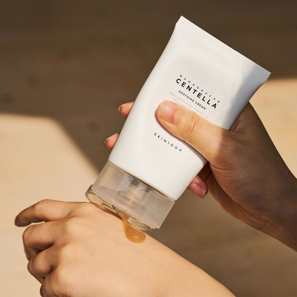SKIN1004 Madagascar Centella Soothing Cream tube dispensing amber gel onto the back of a hand