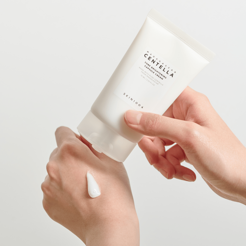 Tubo de SKIN1004 Tone Brightening Capsule Cream sobre una gota de crema blanca en el dorso de una mano